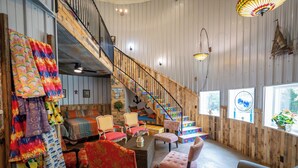 A spacious room with a wooden staircase, multiple seating areas, and large windows providing natural light. - Sleeps 6 in a 2-story grain bins 2 queen beds 1 queen bunk & 2 full bathrooms. (Hermann)