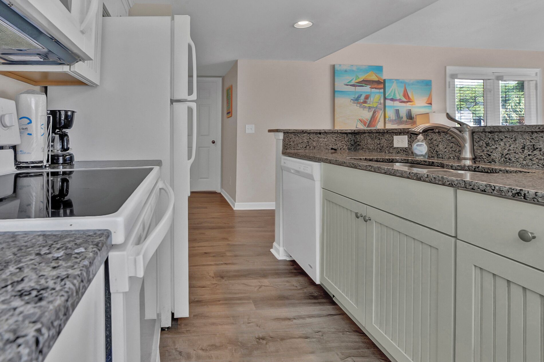 A kitchen with white cabinets, granite countertops, and a dishwasher. There are two paintings on the wall depicting sailboats.