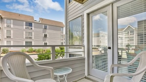 Un balcon avec deux chaises blanches et une petite table, donnant sur un quartier résidentiel avec des maisons et un ciel dégagé.