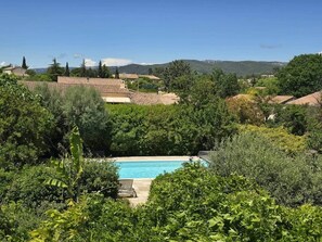A swimming pool surrounded by lush greenery and houses with red-tiled roofs.