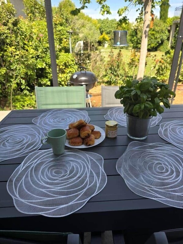 A table with placemats, a plate of pastries, a green mug, a potted plant, and a jar of jam.