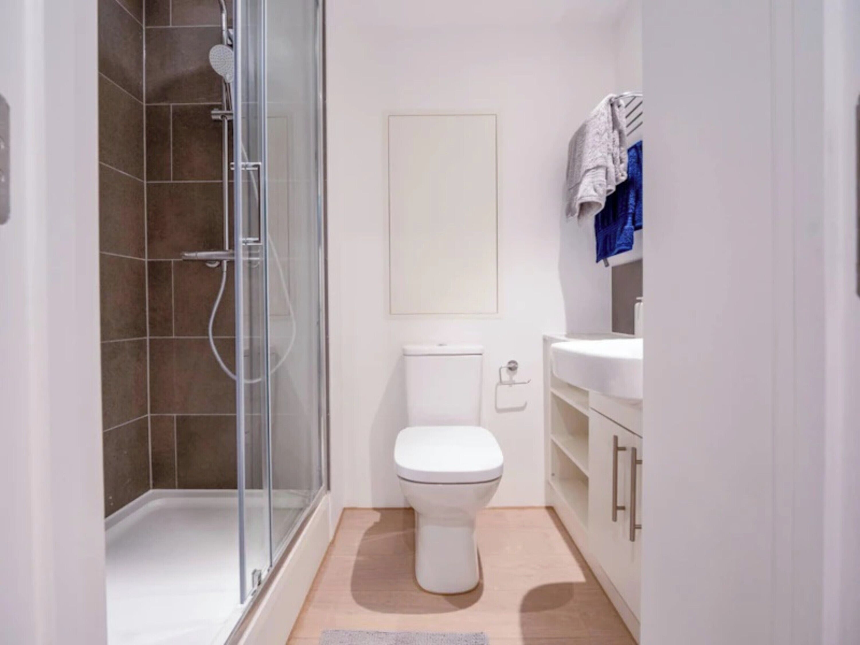 A modern bathroom with a glass shower enclosure, a white toilet, and a sink with a towel rack.