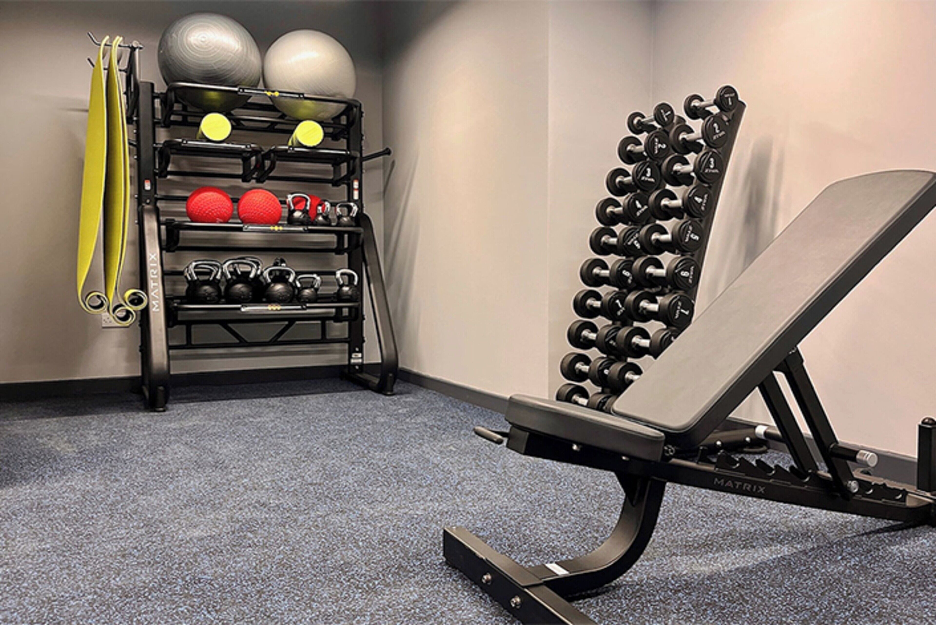A gym with a bench press, kettlebells, and a rack of dumbbells.