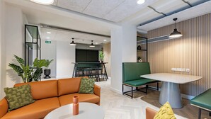 A modern office space with a green sofa, a round table, and a dining area with a green bench. - Student Only, Elegant Bronze Studio in Paddington (London)