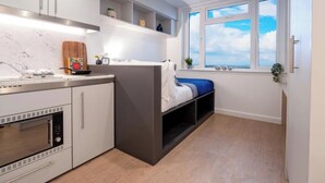 A compact kitchen with a built-in oven, a microwave, and a window with a view of the sky. - Student Only, Elegant Bronze Studio in Paddington (London)