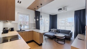 A modern kitchen with a built-in island, a dining area with a round table, and a seating area with a sofa. - Rezydencja Willora Świnoujście (Swinoujscie)