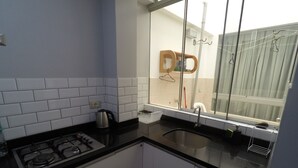 A compact kitchen with white cabinets, a black countertop, a gas stove, and a window with a view of a balcony. - Apartment 5 minutes from downtown (Paracas)