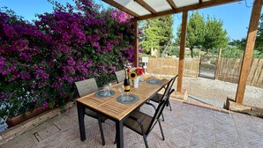 Une terrasse extérieure avec une table et des chaises en bois, entourée d’une pergola et agrémentée de magnifiques fleurs de bougainvillier aux couleurs violettes éclatantes.