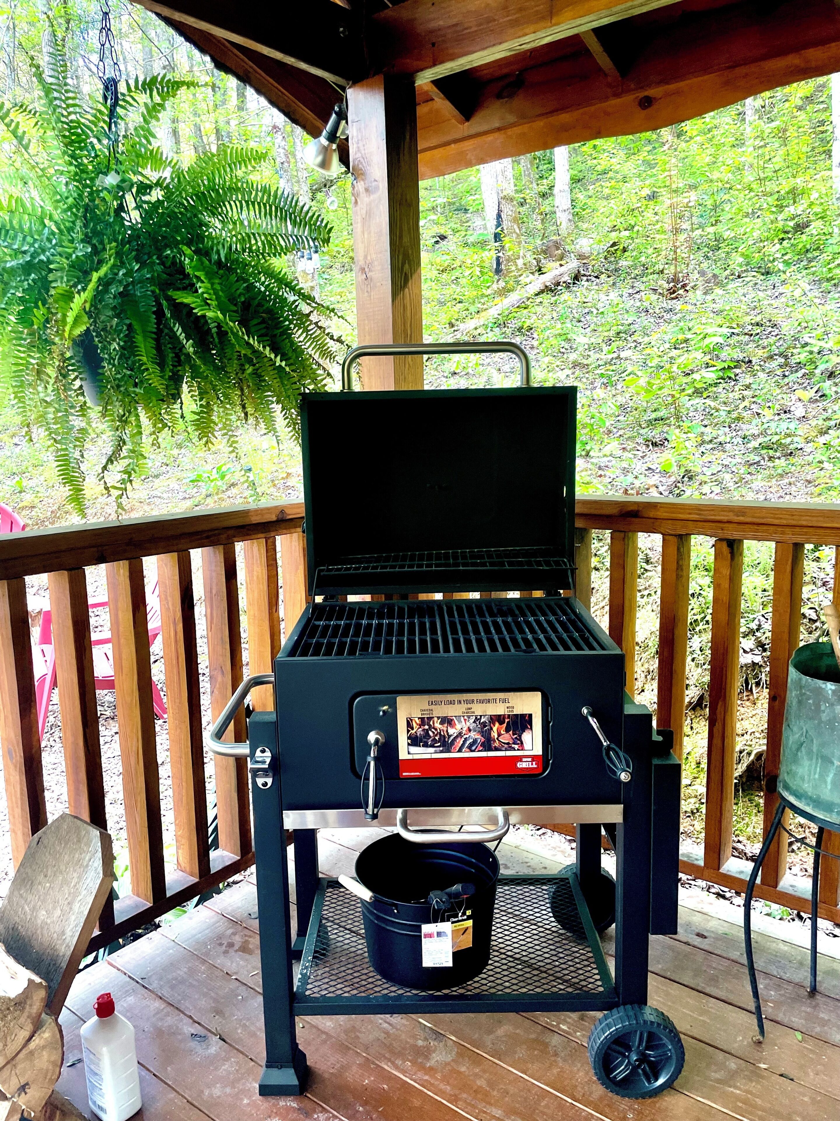 A portable barbecue grill with a fuel tank and a metal bucket on a wooden deck.