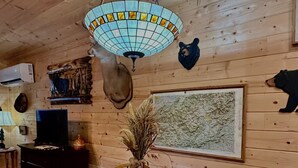 Un intérieur en bois avec une table de salle à manger ronde, des sets de table à motifs d’ours, une lampe suspendue et des têtes d’animaux fixées au mur.