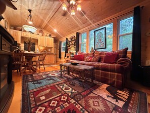 A cozy cabin interior with a wooden dining table, a plaid sofa, and a patterned rug. - Little Bear Tiny Cabin in The Forest (Cosby)