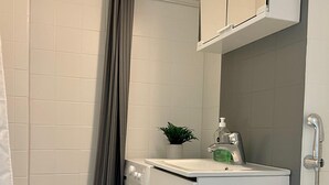 A compact bathroom with a washing machine, a small sink with a soap dispenser, and a shower area with a curtain.