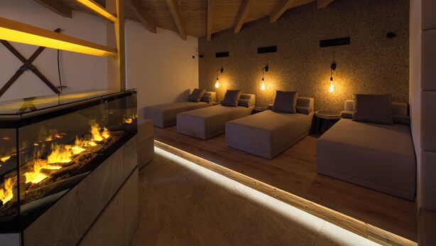 Ein moderner Spa-Raum mit Kamin aus Glas, Holzbalken und drei Sitzbereichen mit Wandleuchten.