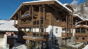 Eine Holzhütte mit Balkonen, einem Schild mit der Aufschrift 'Der Zimhof' und einer verschneiten Landschaft.