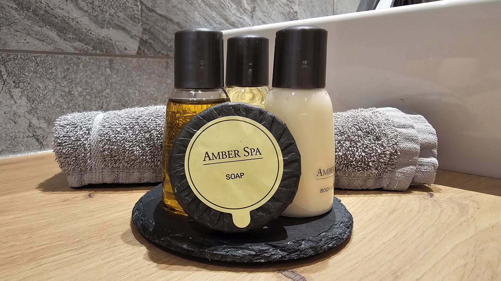 Trois bouteilles de savon sur un sous-verre en ardoise, avec des serviettes en arrière-plan.