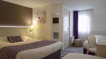 Une chambre d’hôtel avec un grand lit, un bureau avec une chaise, une petite table, un miroir et une fenêtre avec des rideaux.