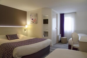 Una habitación de hotel con una cama grande, un escritorio con silla, una mesita, un espejo y una ventana con cortinas.