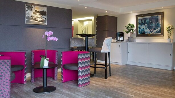 Eine moderne Hotelhalle mit lebendigen pinkfarbenen Sitzgelegenheiten, einer Kaffeestation und Kunstwerken an den Wänden.
