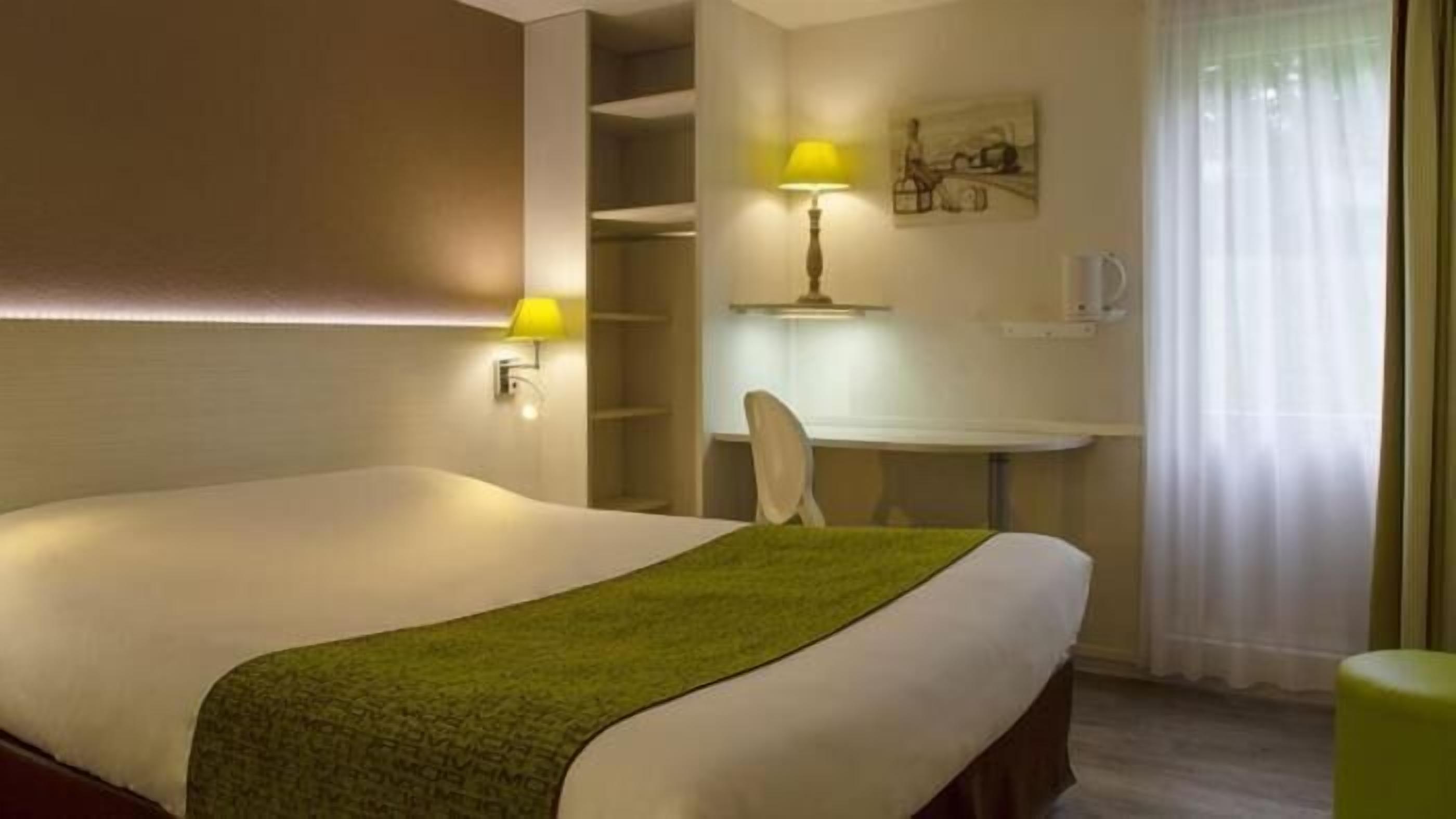 Quarto de hotel com uma cama, uma escrivaninha e uma cadeira.