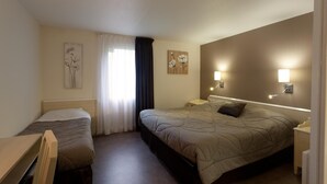 Habitación de hotel con cama individual, escritorio y silla. Hay dos lámparas de pared y un cuadro en la pared.