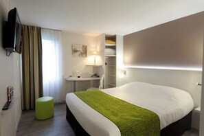 Habitación de hotel con cama, escritorio, silla, televisor y ventana con cortinas.