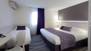 Habitación de hotel con dos camas, un escritorio, una silla y un ventanal con cortinas.