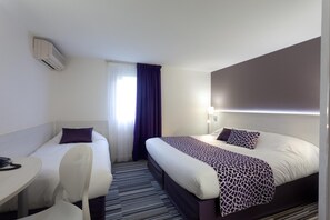 Habitación de hotel con dos camas, un escritorio, una silla y un ventanal con cortinas.