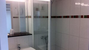 Un baño con ducha de vidrio, un lavabo blanco y un espejo encima.