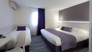 Ein Hotelzimmer mit einem Einzelbett, einem zusätzlichen Bett, einem Schreibtisch mit Stuhl und einem Fenster mit Vorhängen.