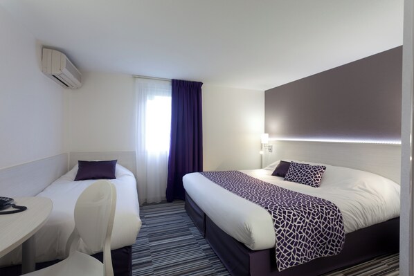 Habitación de hotel con una cama individual, una cama más pequeña, un escritorio con silla y una ventana con cortinas.