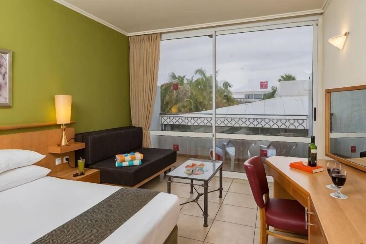 Une chambre d’hôtel avec un lit, un canapé, une petite table, une chaise, un balcon avec vue et une fenêtre avec des rideaux.
