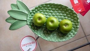 En grön tallriksformad dekoration i form av en ananas, med tre gröna äpplen placerade på den, stående på ett klinkergolv.