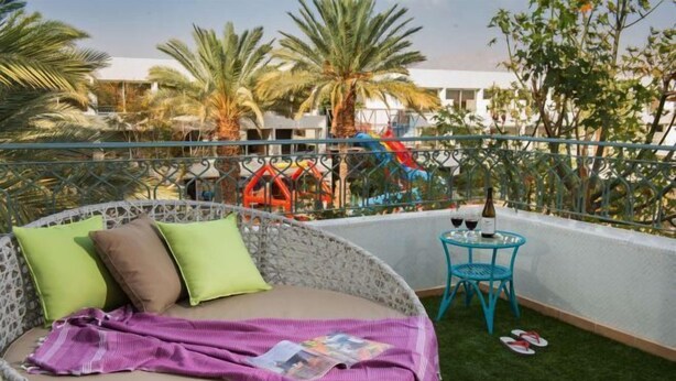 A balcony with a wicker chair, a small table, and a glass bottle. - Leonardo Club Eilat - All Inclusive (Eilat)