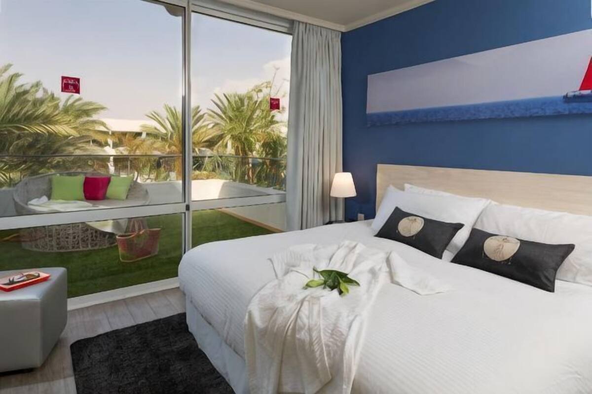 Une chambre d’hôtel avec un grand lit, une vue sur les palmiers et un balcon avec une chaise.