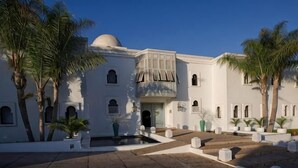 Un bâtiment blanc surmonté d’un dôme, doté de nombreuses fenêtres et d’une cour intérieure agrémentée de palmiers.