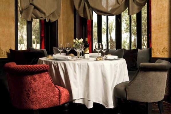 A dining area with a round table set for two, featuring a white tablecloth, wine glasses, and a vase with flowers. - Le Riad Villa Blanche (Agadir)