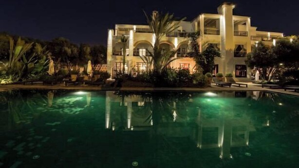 Un hôtel à plusieurs étages doté d’une piscine, entouré de plantes tropicales et illuminé la nuit.