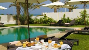 Un coin petit-déjeuner aménagé au bord de la piscine, avec des parasols, des chaises longues et une vue sur la mer.
