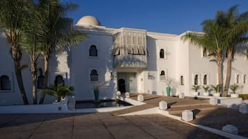A white building with a dome, multiple windows, and a courtyard with palm trees.