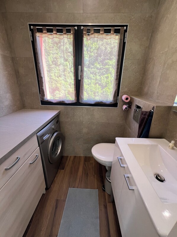 Une petite salle de bain équipée d’un lave-linge, de toilettes et d’une baignoire.