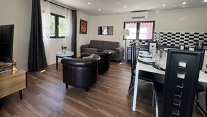 A modern living room with a sofa, a dining table set for four, a television, and a kitchen area with a checkered backsplash. - T4 air-conditioned duplex with terrace, jacuzzi & parking - near Nice & Monaco (La Trinité)