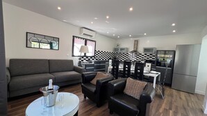 A modern living room with a sofa, two armchairs, a glass coffee table, and a kitchen area with a refrigerator, microwave, and stove. - T4 air-conditioned duplex with terrace, jacuzzi & parking - near Nice & Monaco (La Trinité)