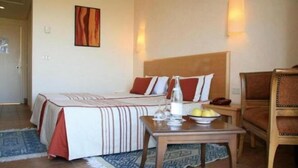 A hotel room with a bed, a bedside table with a glass of water and fruit, a chair, and a wall-mounted artwork. - Sufetula Hotel (Sbeitla)