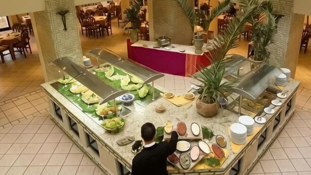 A buffet with various food items and a staff member attending to it. - Sufetula Hotel (Sbeitla)