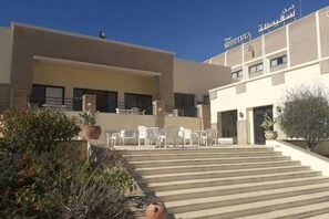 A building with a staircase leading to a door, outdoor seating, and potted plants. - Sufetula Hotel (Sbeitla)