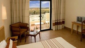 A hotel room with a bed, a sofa, a small table, a TV, and a balcony with a view. - Sufetula Hotel (Sbeitla)