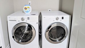 Un lavadero con dos lavadoras LG blancas de carga frontal y una botella de detergente Tide en un estante.