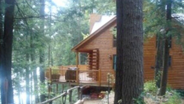 Une cabane dotée d’une terrasse en bois et d’un porche abrité, entourée d’arbres.