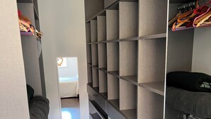 Un vestidor amplio con varios estantes y espacio para colgar, una cama al fondo y piso de madera.