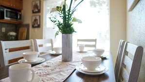 Et spisebord med hvide kopper og underkopper, en vase med blomster og træstole.
